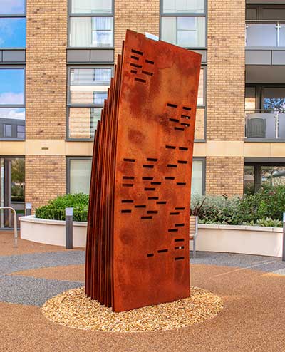 Curved sculpture in oxidised mild steel of five panels with laser cutouts that reference formal written letters