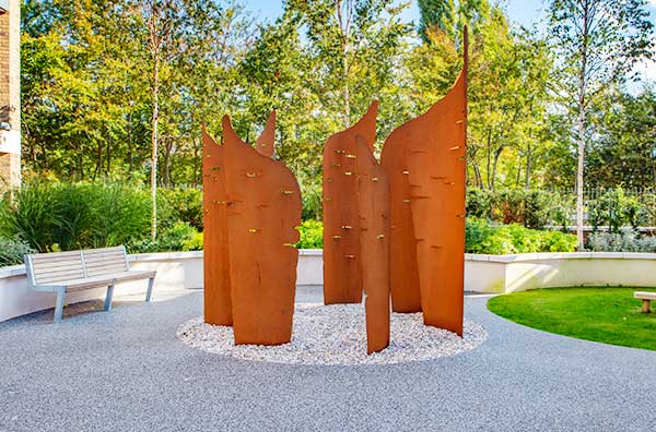 Curved sculpture in oxidised mild steel of five panels with laser cutouts that reference formal written letters
